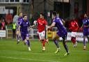 Swindon Town's George McEachran (red) tries to dribble away from former Robins midfielder Jake Reeves (purple - left)