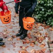 Two children holding pumpkin buckets while they go trick or treating. Credit: Canva